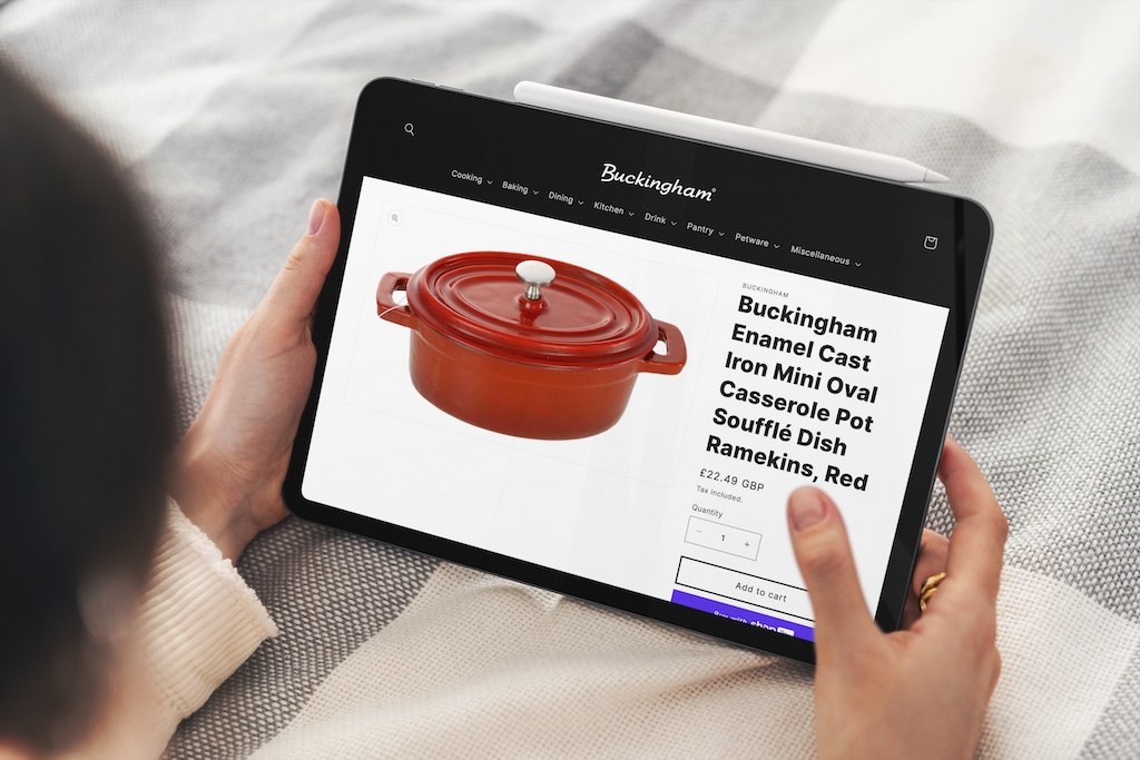 A woman holding an iPad looking closely at a Buckinghm Cookware casserole pot.